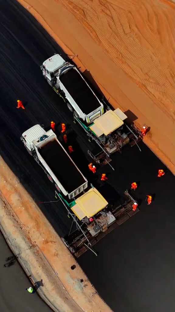 Aerial view of FALA Road crews paving asphalt with two pavers and tipper trucks